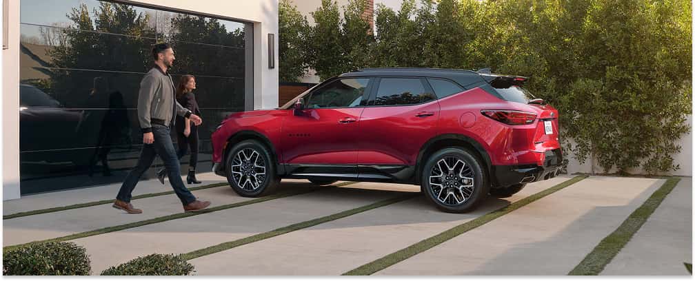 Rear three-quarter view of a red 2026 Chevrolet Blazer with a black roof parked on a residential driveway.
