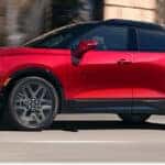 Front three-quarter view of a red 2026 Chevrolet Blazer with a black roof driving on a city street.