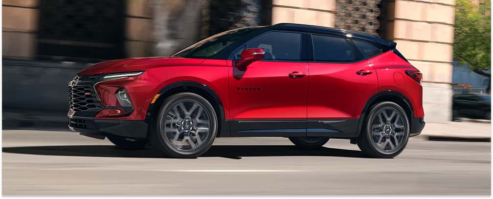 Front three-quarter view of a red 2026 Chevrolet Blazer with a black roof driving on a city street.