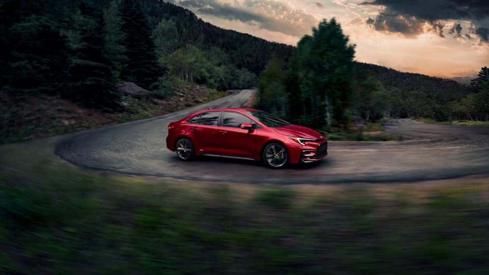 A red 2026 Toyota Corolla sedan driving down a curving wooded road