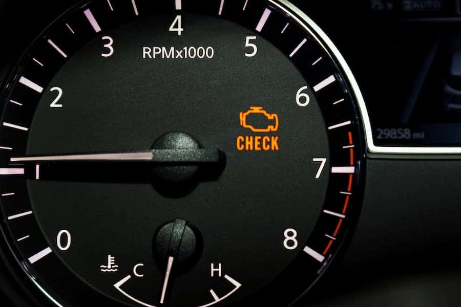 A close up of a vehicle’s dash with the check engine light illuminated in orange