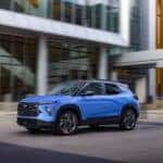 Driver’s side front 3/4 view of 2024 Chevrolet Trailblazer RS in Fountain Blue driving past a building. Preproduction model shown. Actual production model may vary. Available in fall 2023.