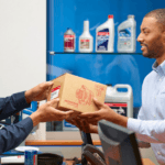 A Honda Service Technician handing a car owner their Honda OEM Parts in the manufacturer packaging.