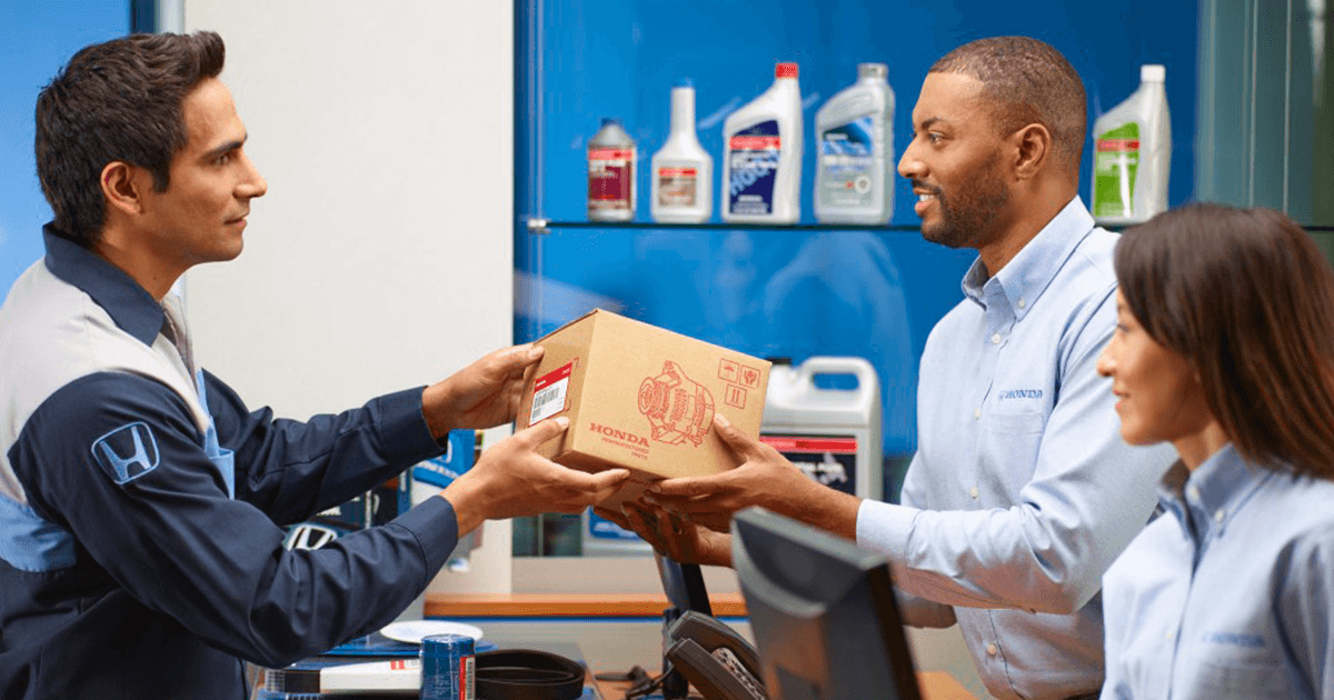 A Honda Service Technician handing a car owner their Honda OEM Parts in the manufacturer packaging.