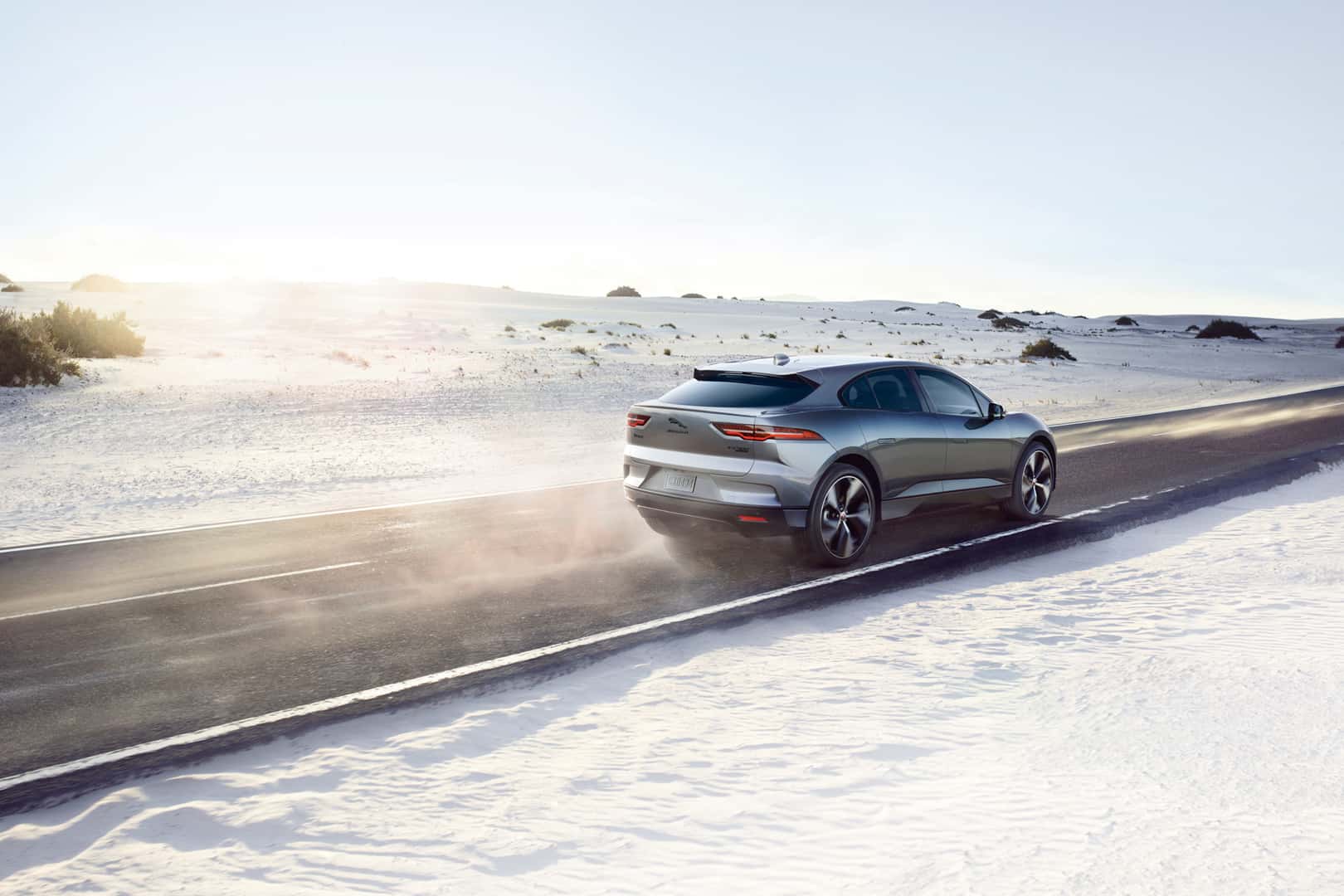 Rear view of Jaguar I-PACE driving on a snowy road at sunrise