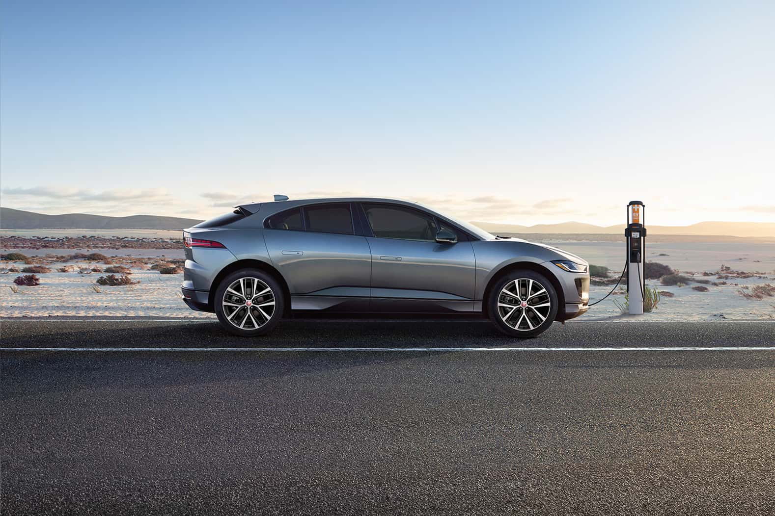 Rear view of Jaguar I-PACE driving on a snowy road at sunrise