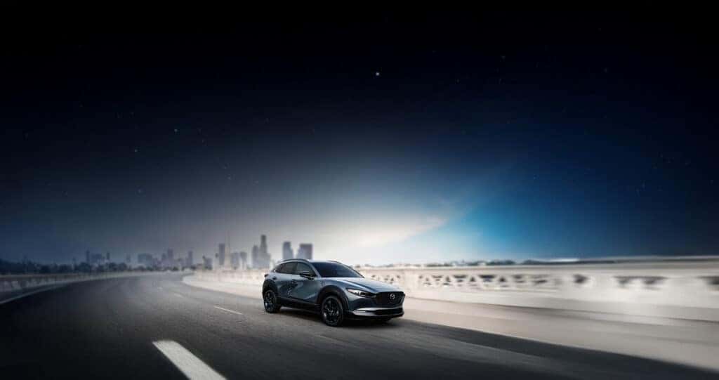 2025-Mazda-CX-30-Driving-over-a-bridge-at-dawn-with-a-city-skyline-in-the-background