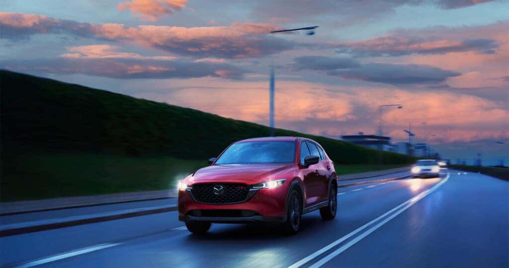 2025 CX-5 DRIVING DOWN THE HIGHWAY WITH A SUNSET AND CLOUDS IN THE BACKGROUND