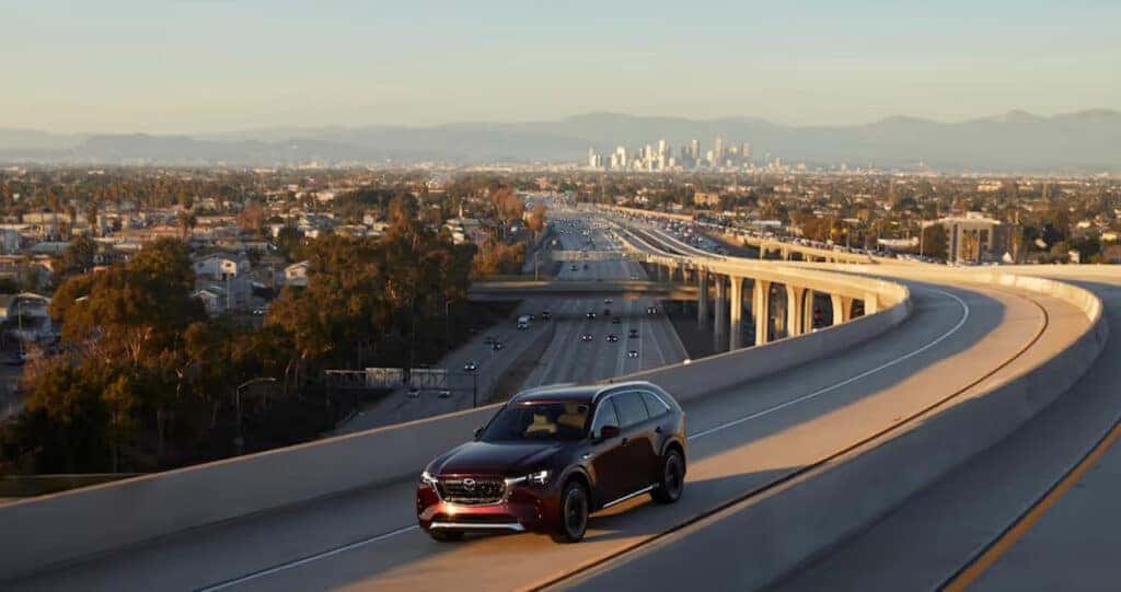 2025-Mazda-CX-90-Driving-on-the-highway-with-the-city-in-the-background