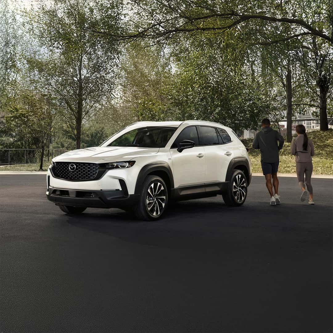 2025 Mazda CX-50 in white parked with a couple jogging around it