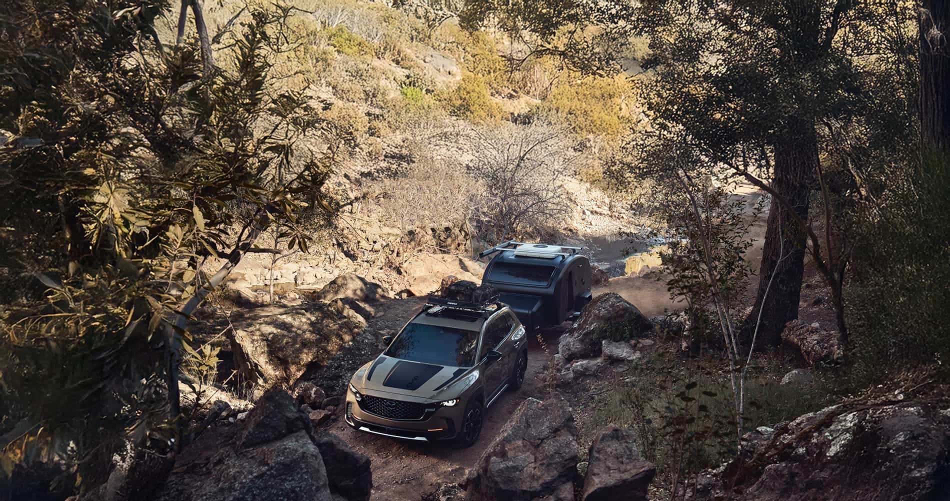Showing the 2026 Mazda CX-50 towing capacity by towing a small teardrop camper up a rugged and rocky offroad trail