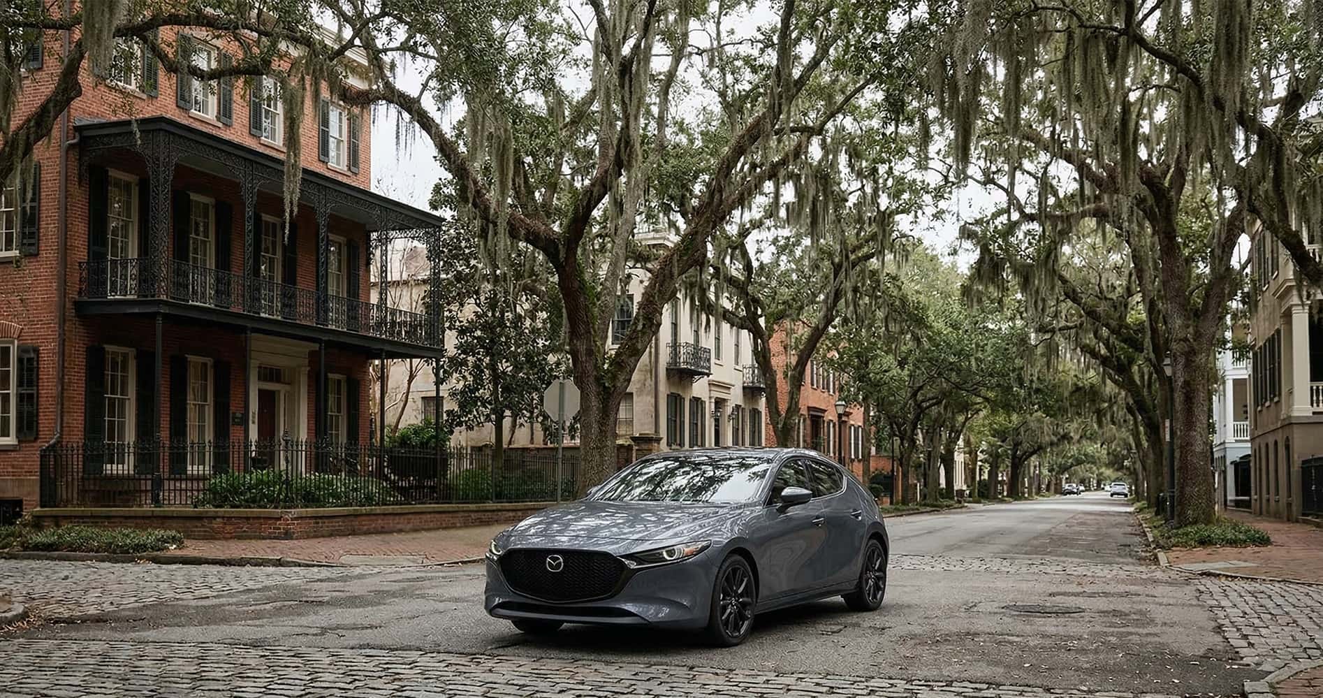 Mazda3 parked on cobblestone street in Savannah GA with historic homes and oak trees