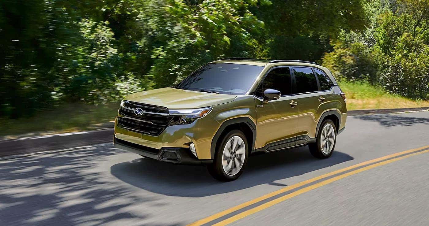 2026 Subaru Forester driving on a tree-lined road with lush greenery, highlighting everyday comfort and visibility