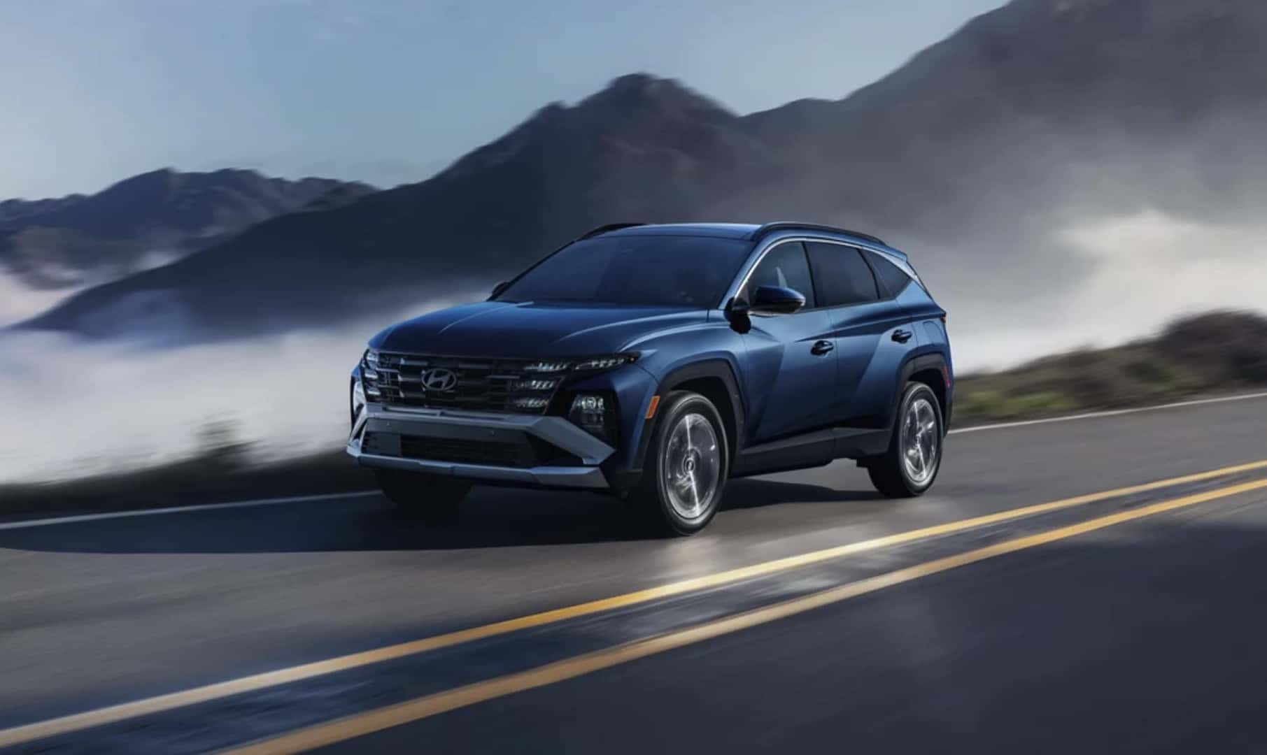 2026 Hyundai Tucson driving on a mountain road with mist and rolling hills in the background