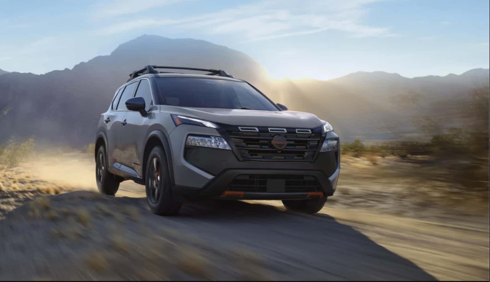 2026 Nissan Rogue driving on a dirt road through a desert landscape with mountains in the background