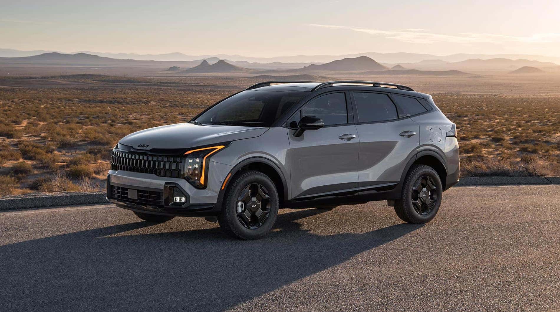 2026 Kia Sportage parked on a desert highway with open landscape and distant mountains at sunset