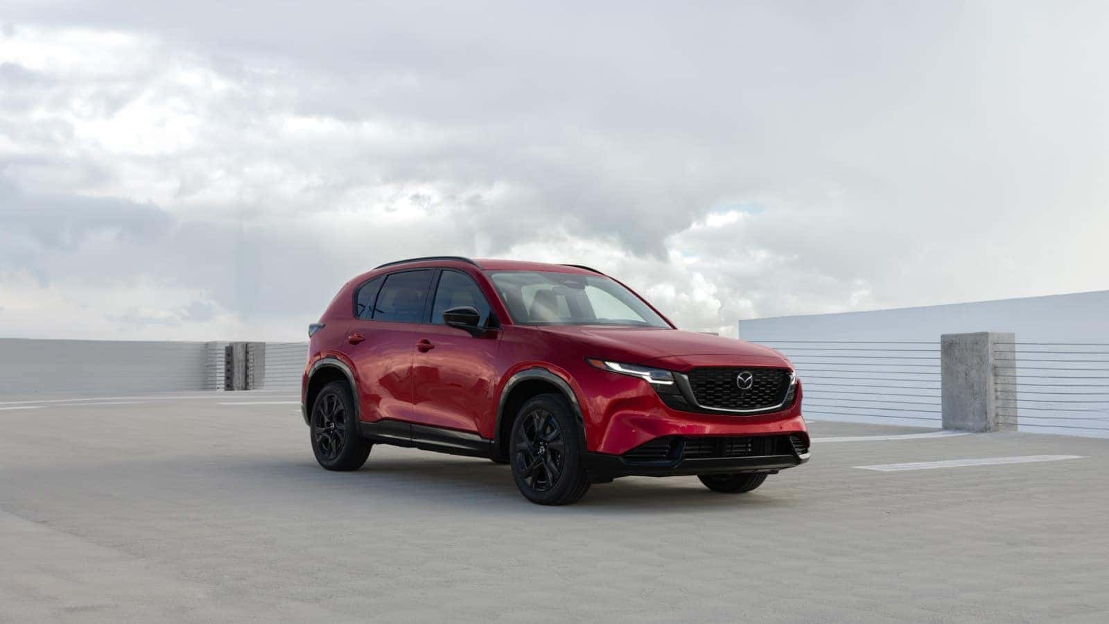 2026 Mazda CX-5 parked on a rooftop parking deck under cloudy skies, showcasing its sleek design and bold red exterior