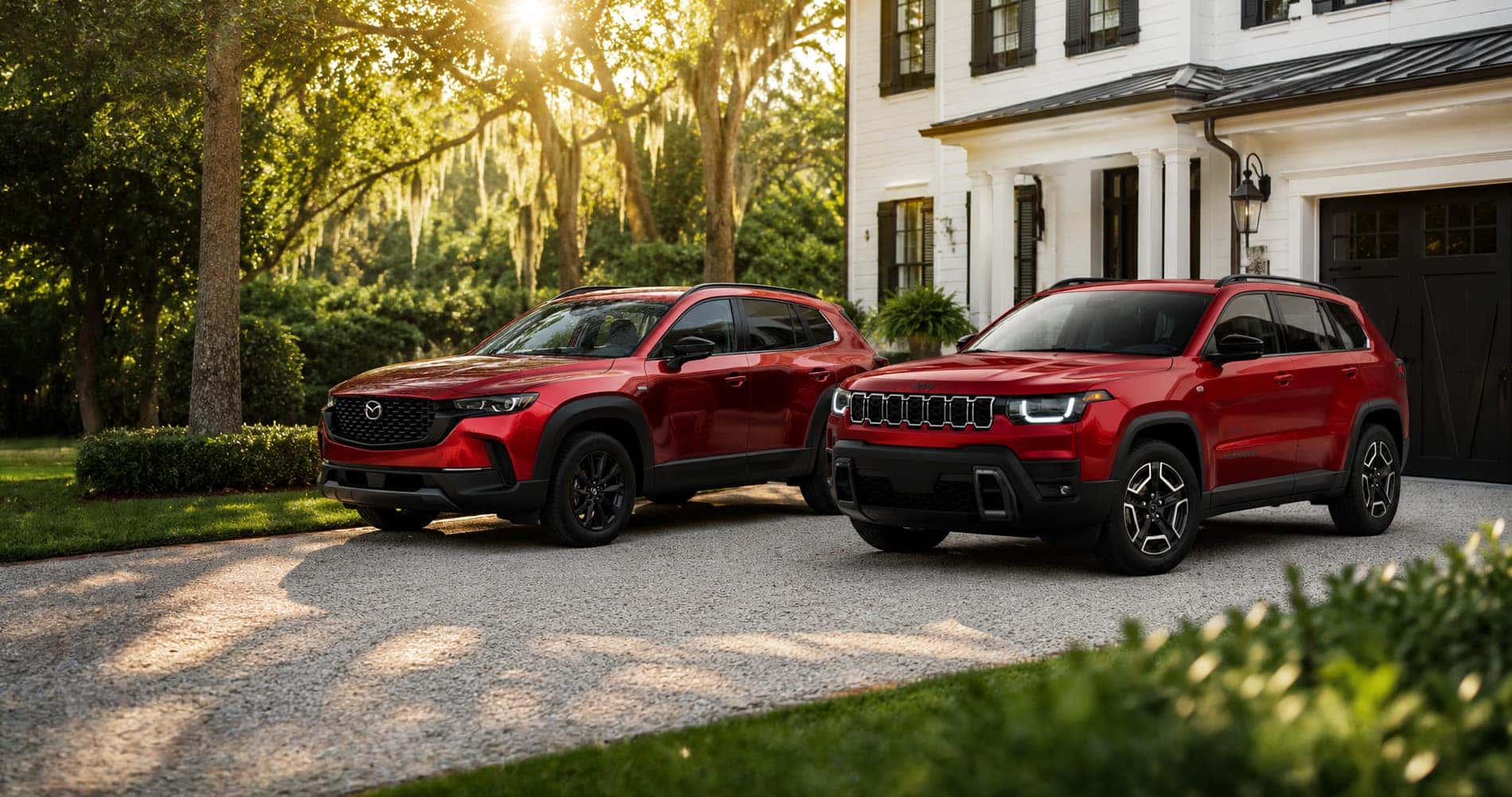 Red Mazda CX-50 Hybrid and red Jeep Cherokee Hybrid SUVs parked in a driveway at sunrise, highlighting design and trim differences.