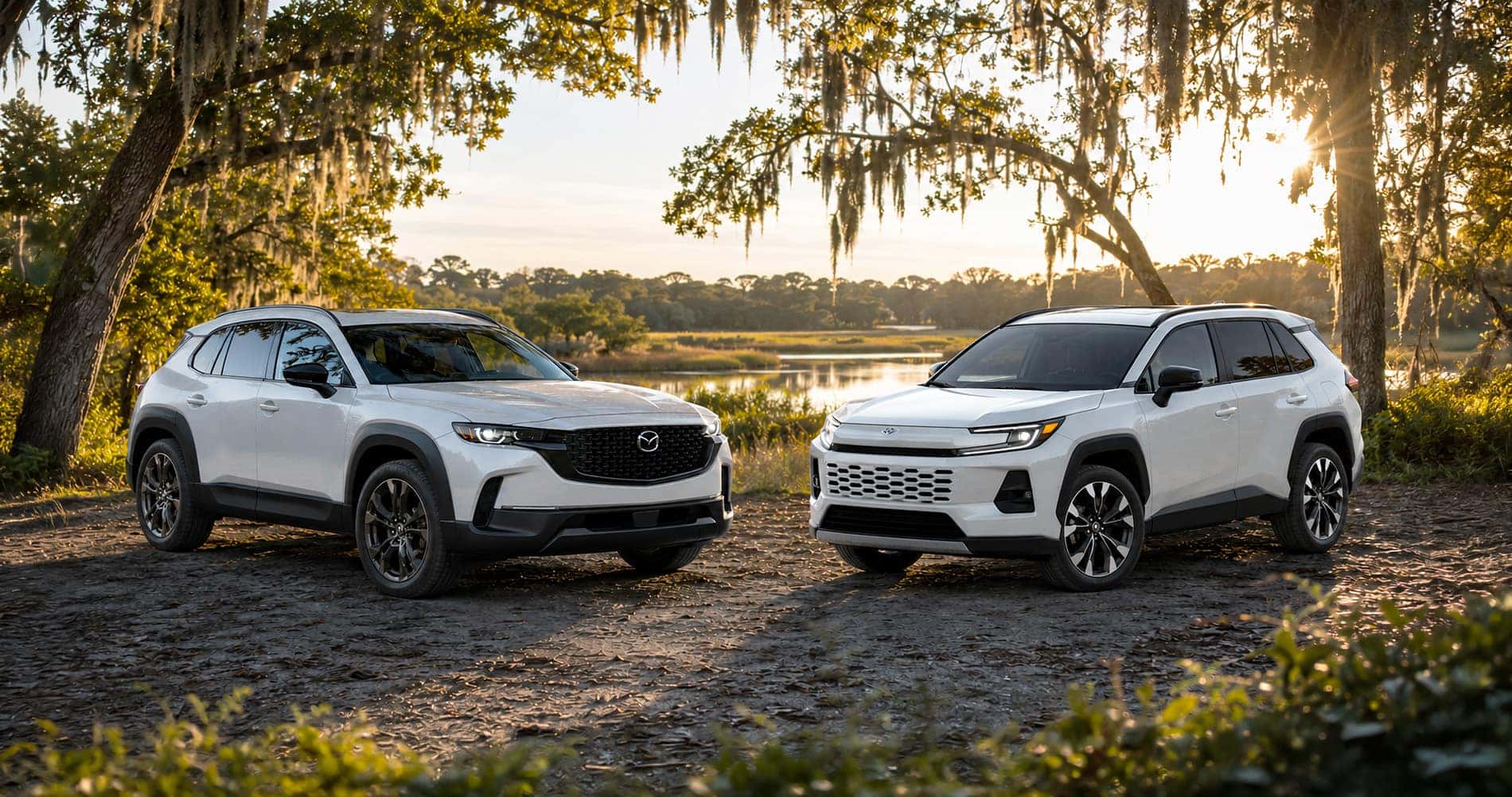 White Mazda CX‑50 Hybrid and white Toyota RAV4 Hybrid parked near river at sunset emphasizing styling and proportions.