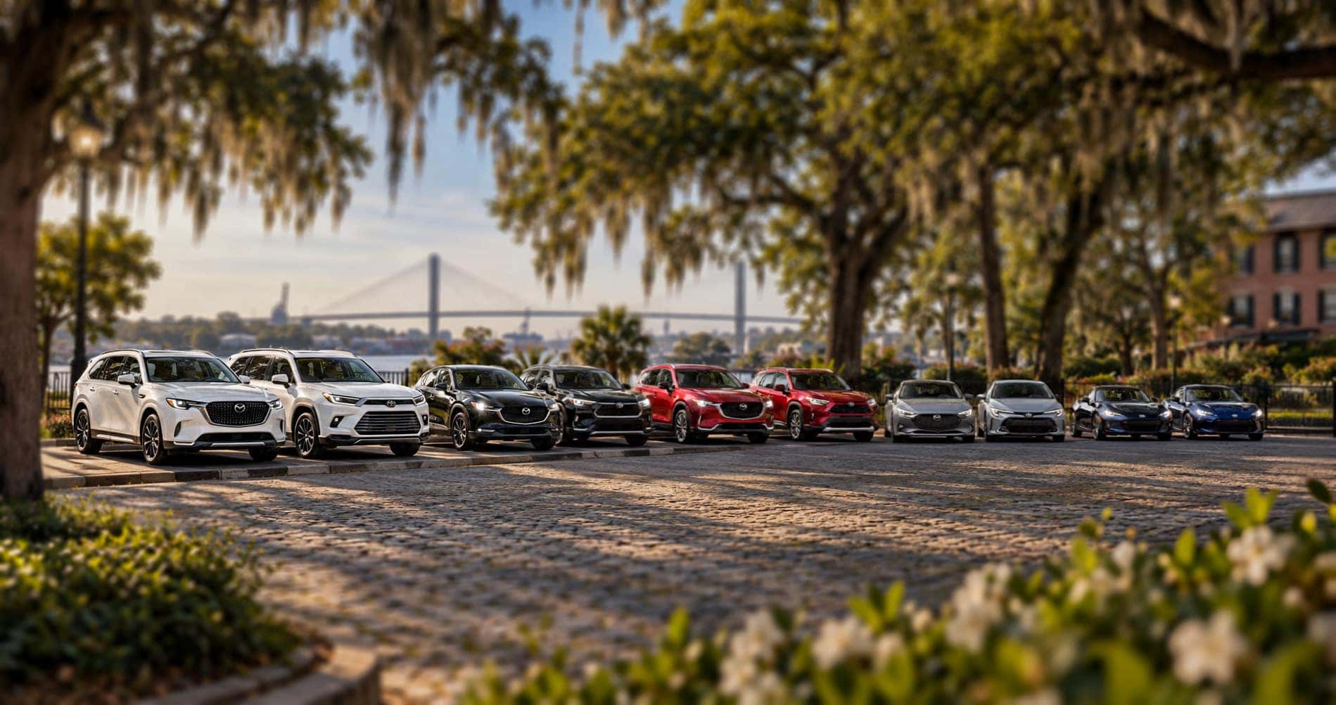 Mazda and Toyota model lineup parked beneath oak trees with the Savannah skyline and bridge in the background