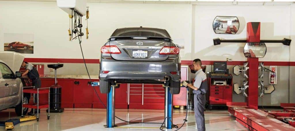 Service Technician using torque gun on tire bolts to a grey Toyota passenger car on a lift