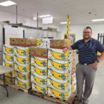 Kalispell Toyota General Manager leaning against a stack of banana boxes full of food inside the flathead food bank