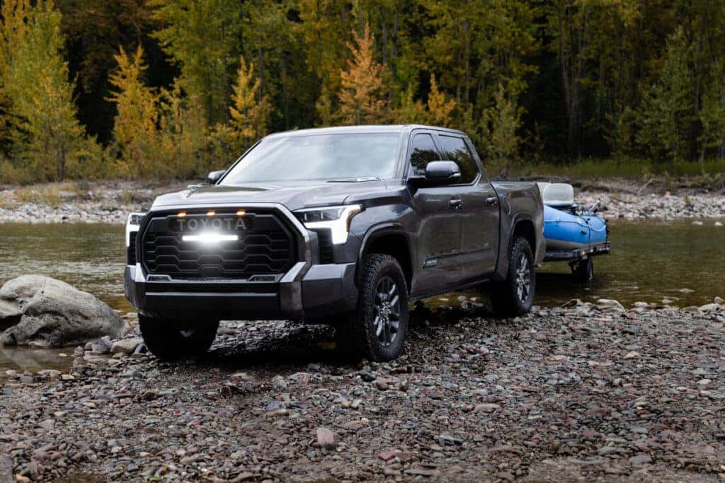 Gray 2023 Toyota Tundra towing a raft near a creek in Glacier National Park