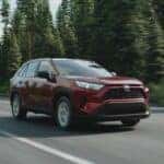 Red Toyota Rav4 LE Hybrid driving on the highway near a forest