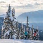 Two skiers stand on top of a snowy mountain overlooking the Flathead Valley