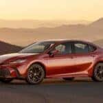 A red 2026 Toyota Camry sits in view with mountains and hills looming in the background