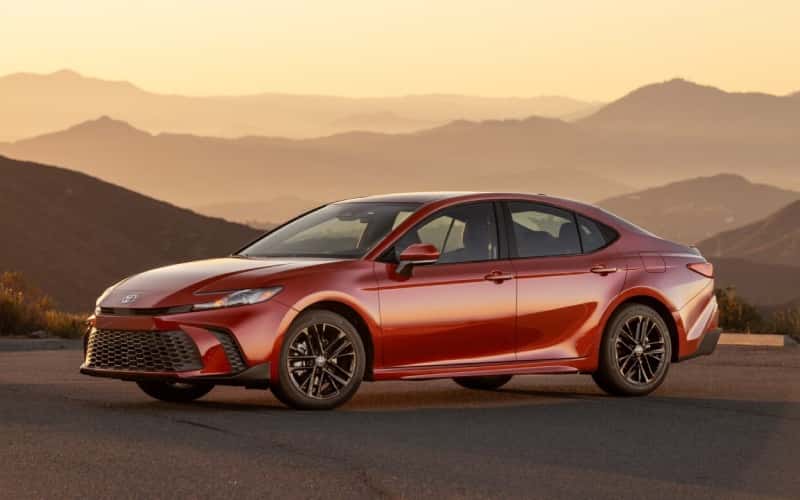 A red 2026 Toyota Camry sits in view with mountains and hills looming in the background