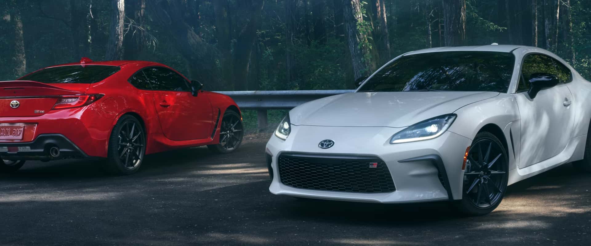 Two 2026 Toyota GR86 sports cars sit on the road with a forest in the background