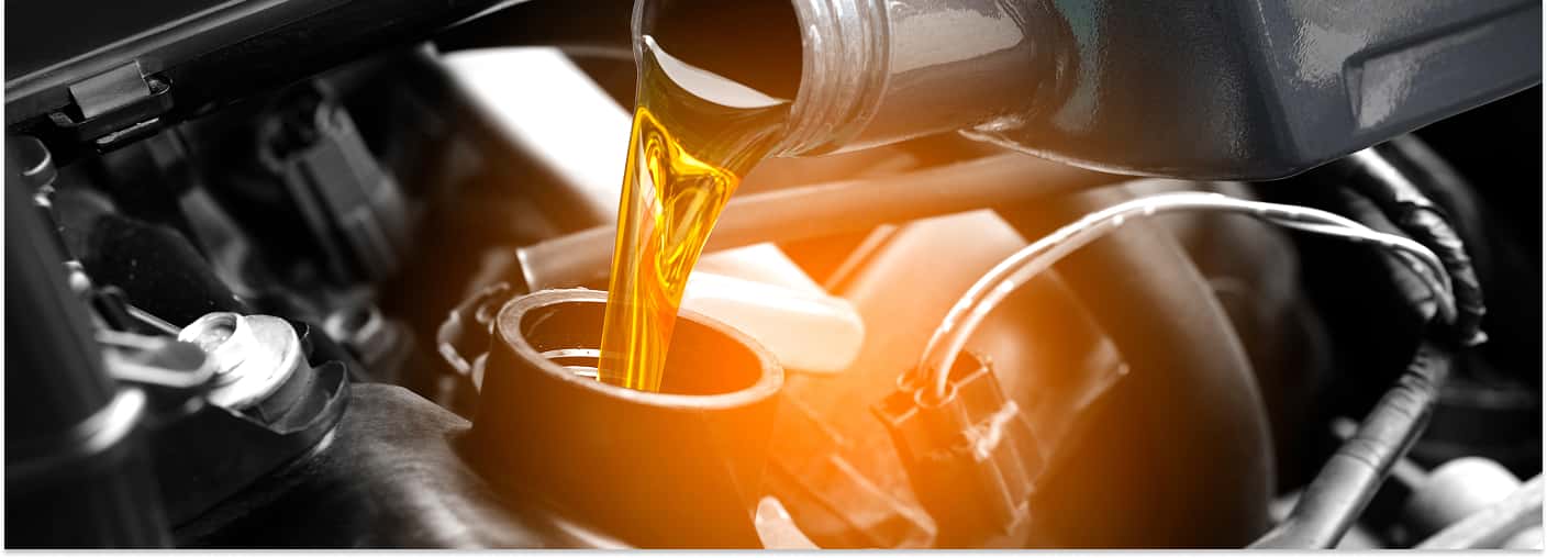 A close-up view of fresh, golden motor oil being poured directly into a vehicle's engine filler opening.