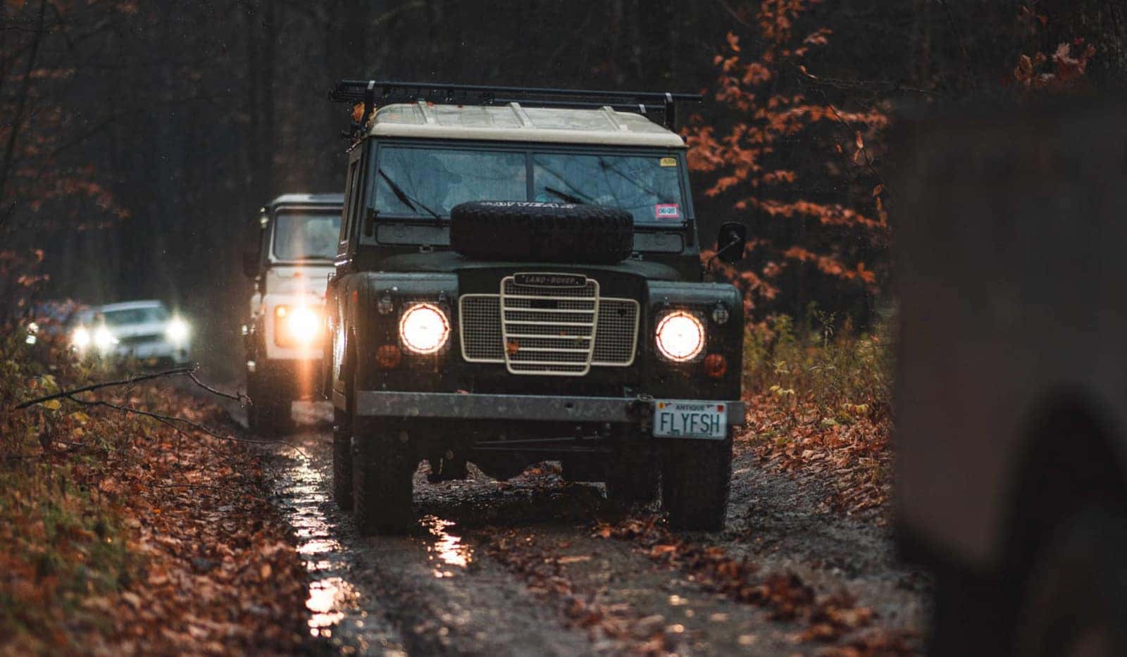 Image of a group of Land Rovers driving offroad through a muddy area.