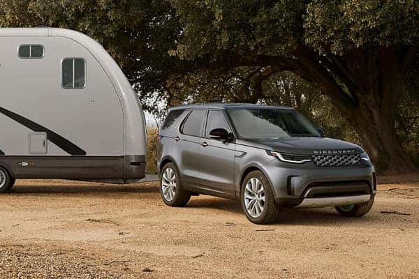 Discovery in silver towing a camper trailer under a large tree