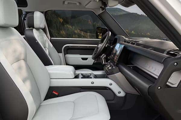 Defender interior with two-tone gray upholstery and open door overlooking forest