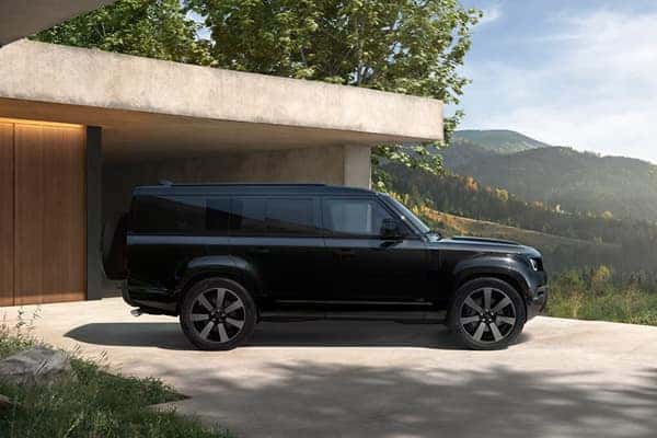 Defender 130 in black side profile parked outside luxury home with mountain view