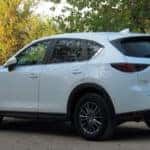 White Mazda CX-5 parked facing toward fall leaves.