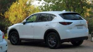 White Mazda CX-5 parked facing toward fall leaves.