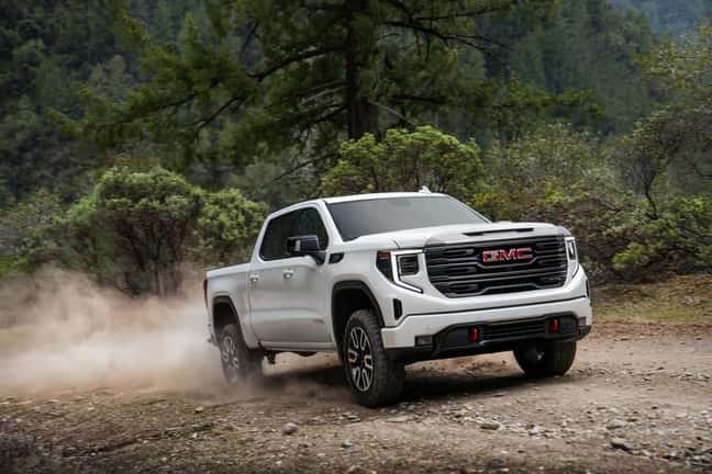 A white GMC Sierra driving on a dirt road in a green forest.