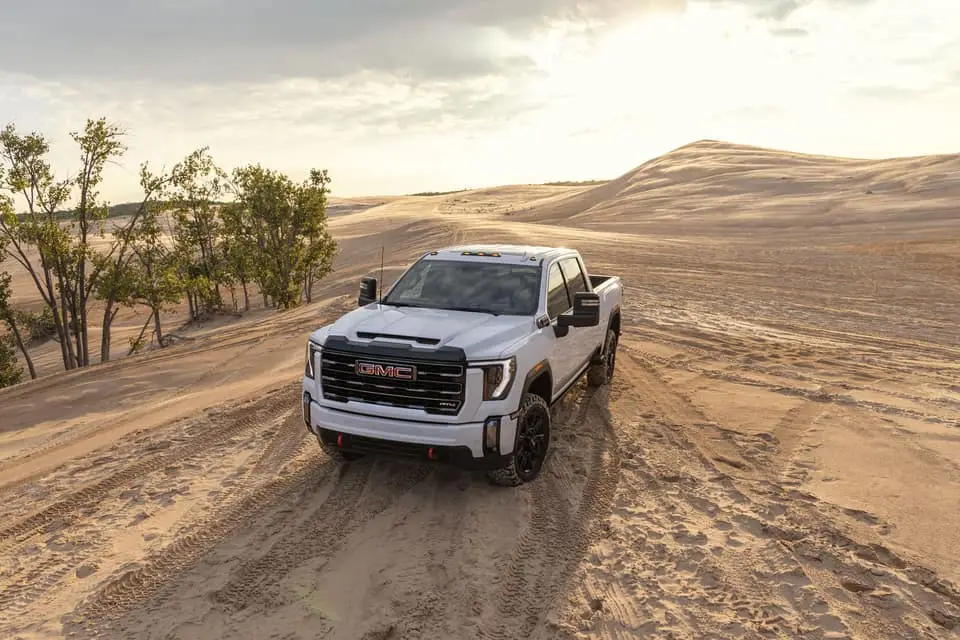 A white GMC Sierra driving in sand dunes in front of a sunrise.