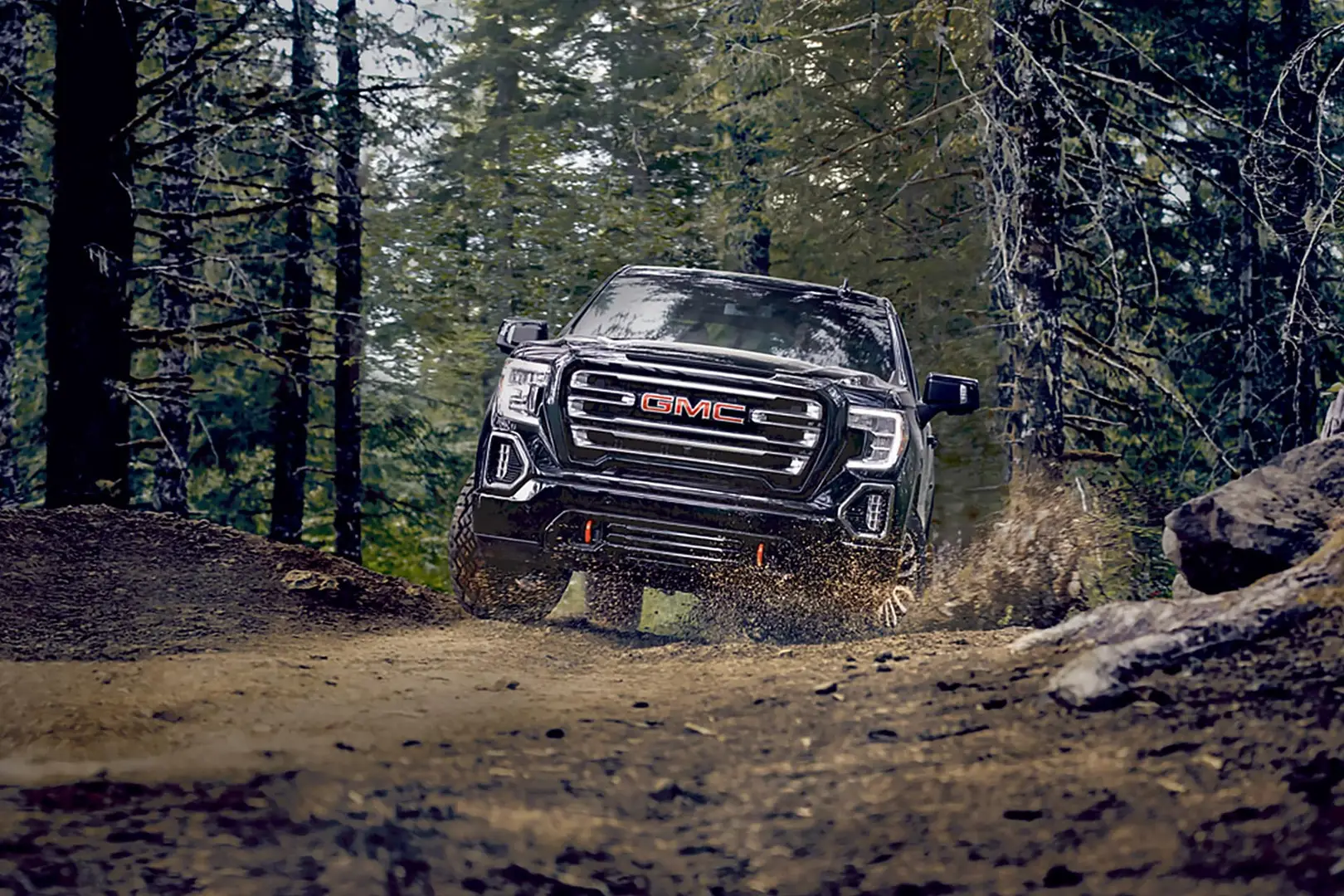 A black GMC Sierra driving off-road in the forest.