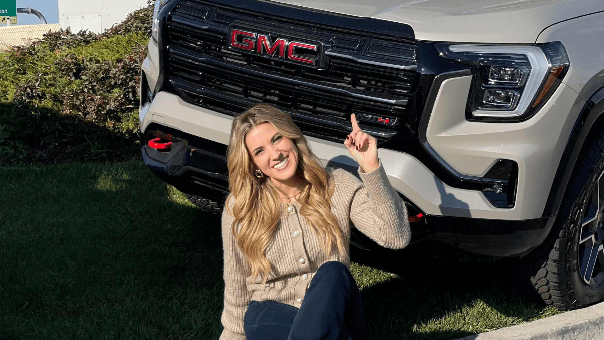 blonde woman pointing up in front of tan GMC