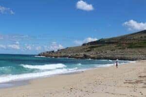 View of the beach from afar with waves crashing on the shore and a hill in the background