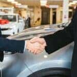 Close of of two men shaking hands in front of a car at the dealership