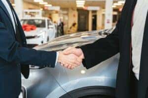 Close of of two men shaking hands in front of a car at the dealership
