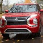 A red Mitsubishi Outlander driving in the rain on a fall day