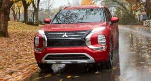 A red Mitsubishi Outlander driving in the rain on a fall day