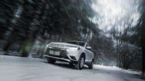 A white Mitsubishi car driving fast on a slippery road in a blizzard 