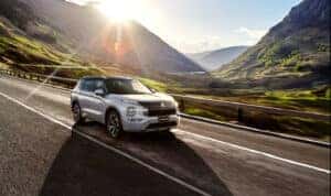 An Outlander PHEV driving down the road with the sun shinning bright behind it.